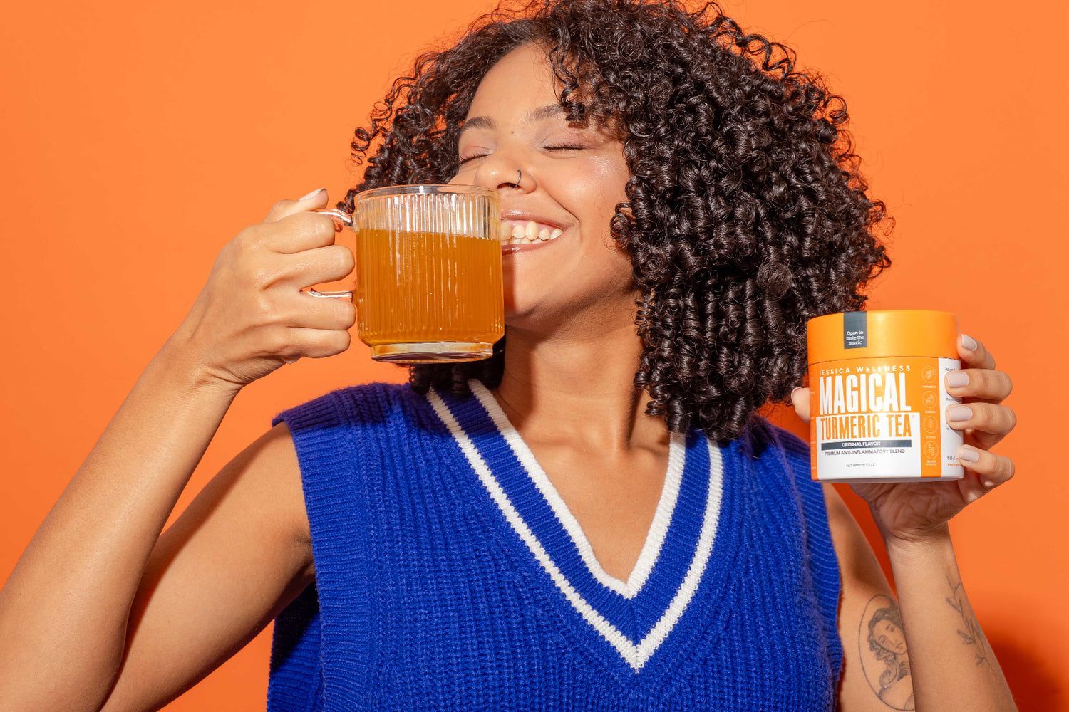 A model with a big smile is showing a glass mug with magical turmeric tea in one hand and the tea canister in the other hand