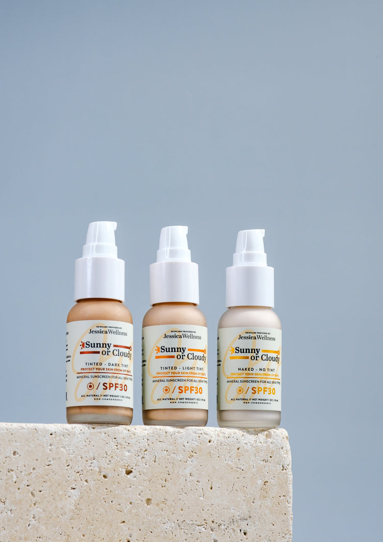 Three bottles of Jessica Wellness Sunny or Cloudy SPF 30 Mineral Sunscreen, featuring dark tint, light tint, and no tint options, displayed on a stone surface against a light blue background.