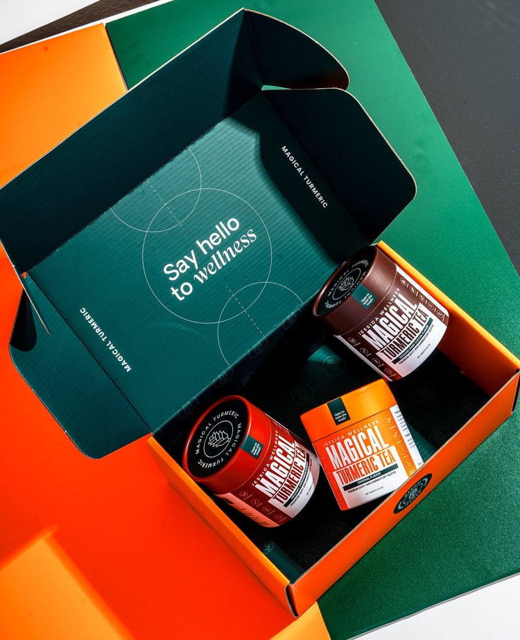 Open box with “Say hello to wellness” inside the lid, containing three jars of Magical Turmeric Tea by Jessica Wellness in vibrant packaging.